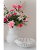 Eine weiße Vase mit einer künstlichen Blume Rhododendron Azalee 73 cm Fuchsia steht neben einer weißen Schale aus gerippter Keramik auf einer glatten Oberfläche vor einem neutralen Hintergrund.