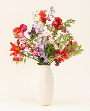 In een vaas met witte structuur staat het Zijden kunstbloemen boeket Pink Pop, met levendige kunstroze bloemen en groene bladeren tegen een lichte achtergrond.
