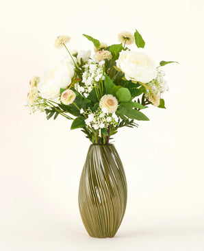 Een groene, geribbelde vaas van keramiek bevat het Zijden kunstbloemen boeket White Love - een arrangement van witte en crèmekleurige bloemen met groene bladeren tegen een effen lichte achtergrond.