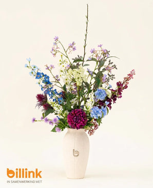 Een witte vaas met de letter b bevat het Zijden kunstbloemen boeket Purple Rain, met blauwe, paarse en witte bloemen. Op de effen lichte achtergrond staat linksonder het logo van billink, met Nederlands vakmanschap.