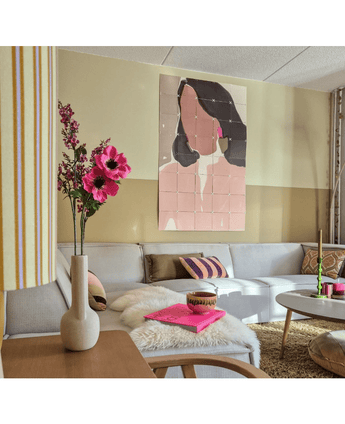 Een gezellige woonkamer met een lichtgrijs bankstel, roze en gouden accenten, een Kunstbloem Anemoon vertakt 56 cm roze in een moderne vaas, een salontafel met een bonten kleed en pastel abstracte kunst van een vrouw aan de muur.