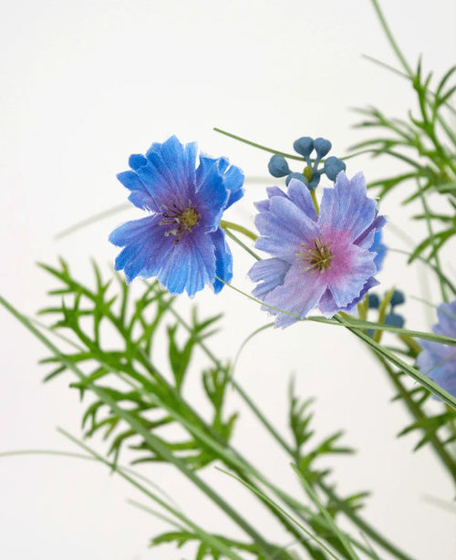 Der Kunstrasen-Zwiebelgrastopf mit Gesangsblumen in Lila (56 cm, feuerfest) hat zarte violette Blüten mit grünen farnartigen Blättern und kleinen runden Knospen vor einem schlichten weißen Hintergrund.