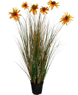 De Kunstgras chrysant uienpot 90cm brandvertragend heeft hoge, groene en bruine grasachtige bladeren met zeven oranje kunstmadeliefbloemen in een zwarte pot, tegen een witte achtergrond.